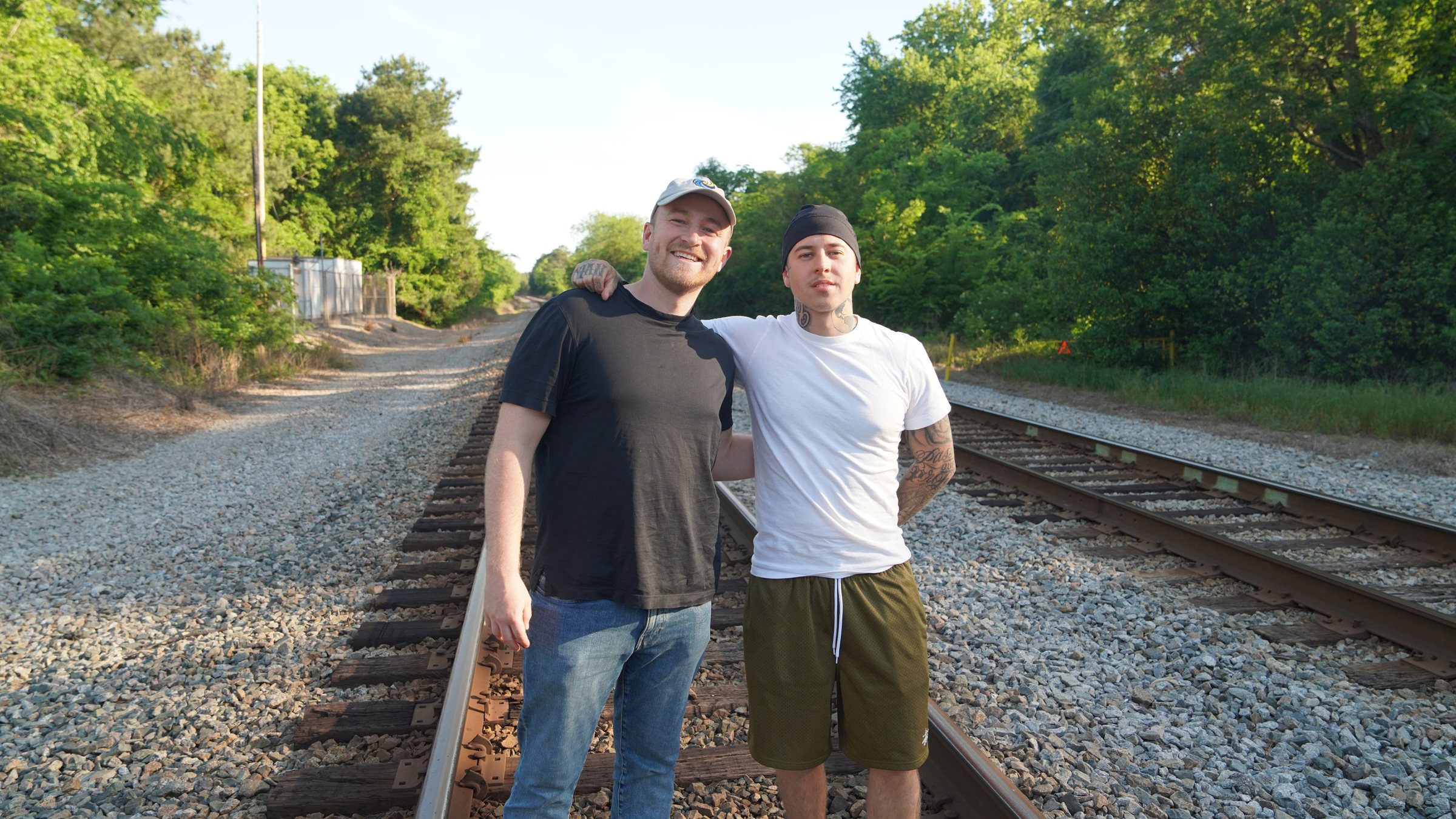 Two people standing together on railroad tracks in late-afternoon light.